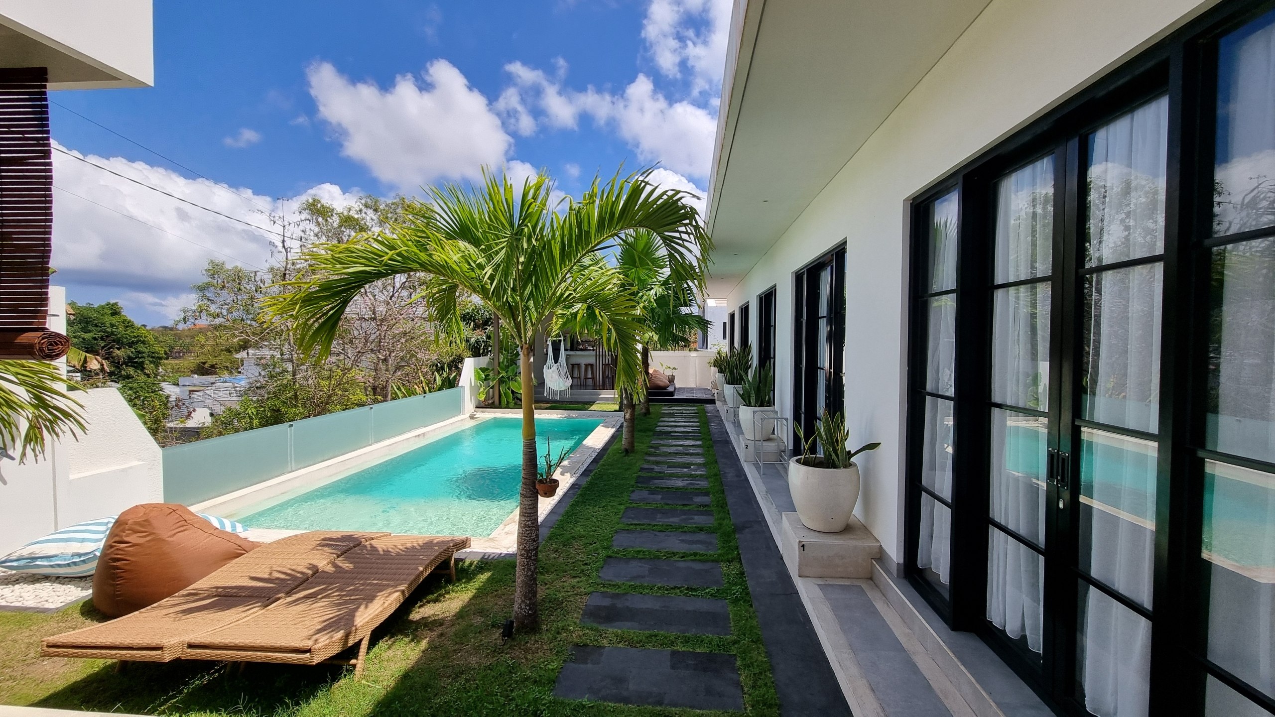 Sun loungers by the pool with the guest rooms along the garden path