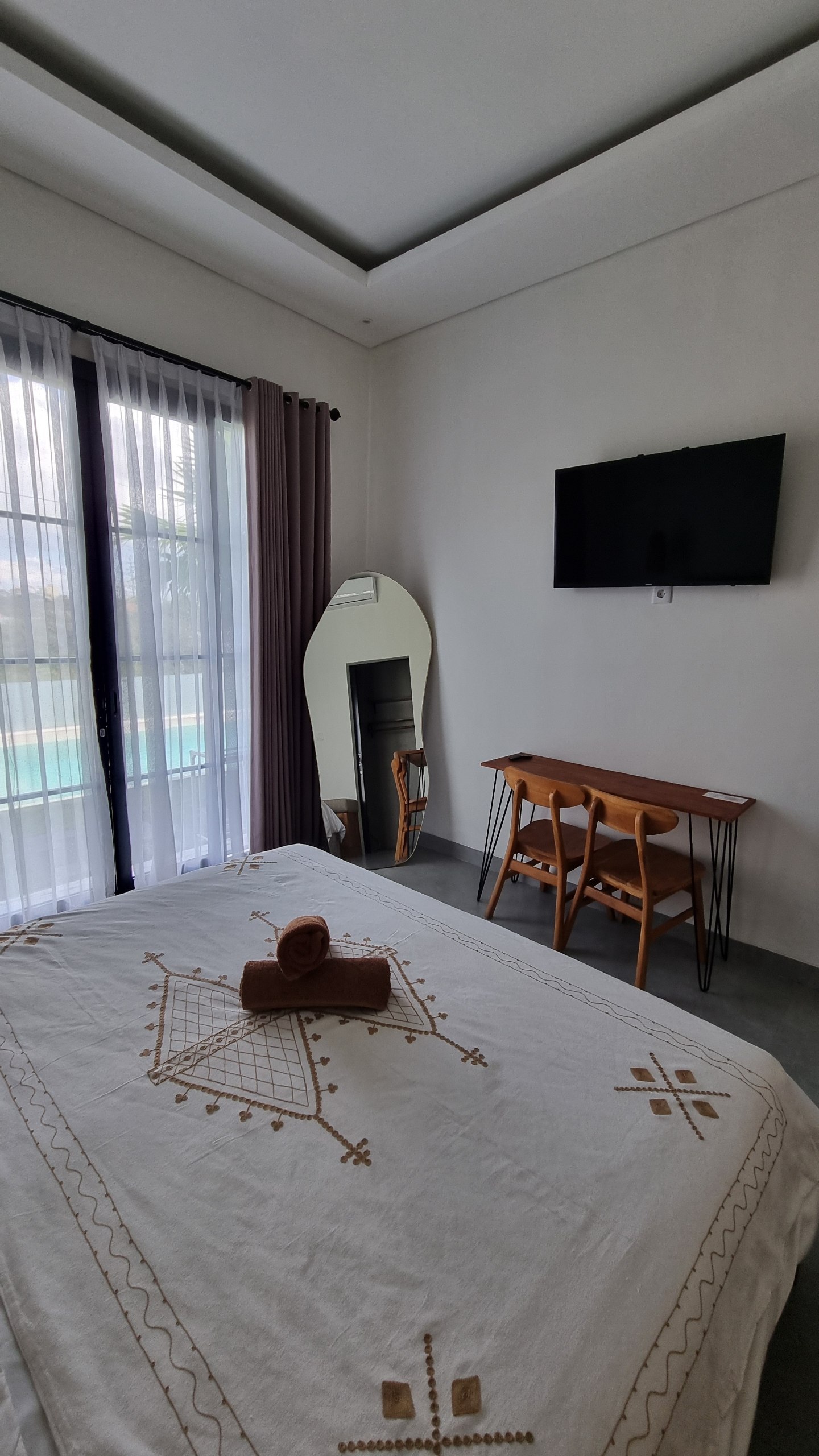 Bedroom with TV, desk, chairs and a curved mirror beside the pool doors