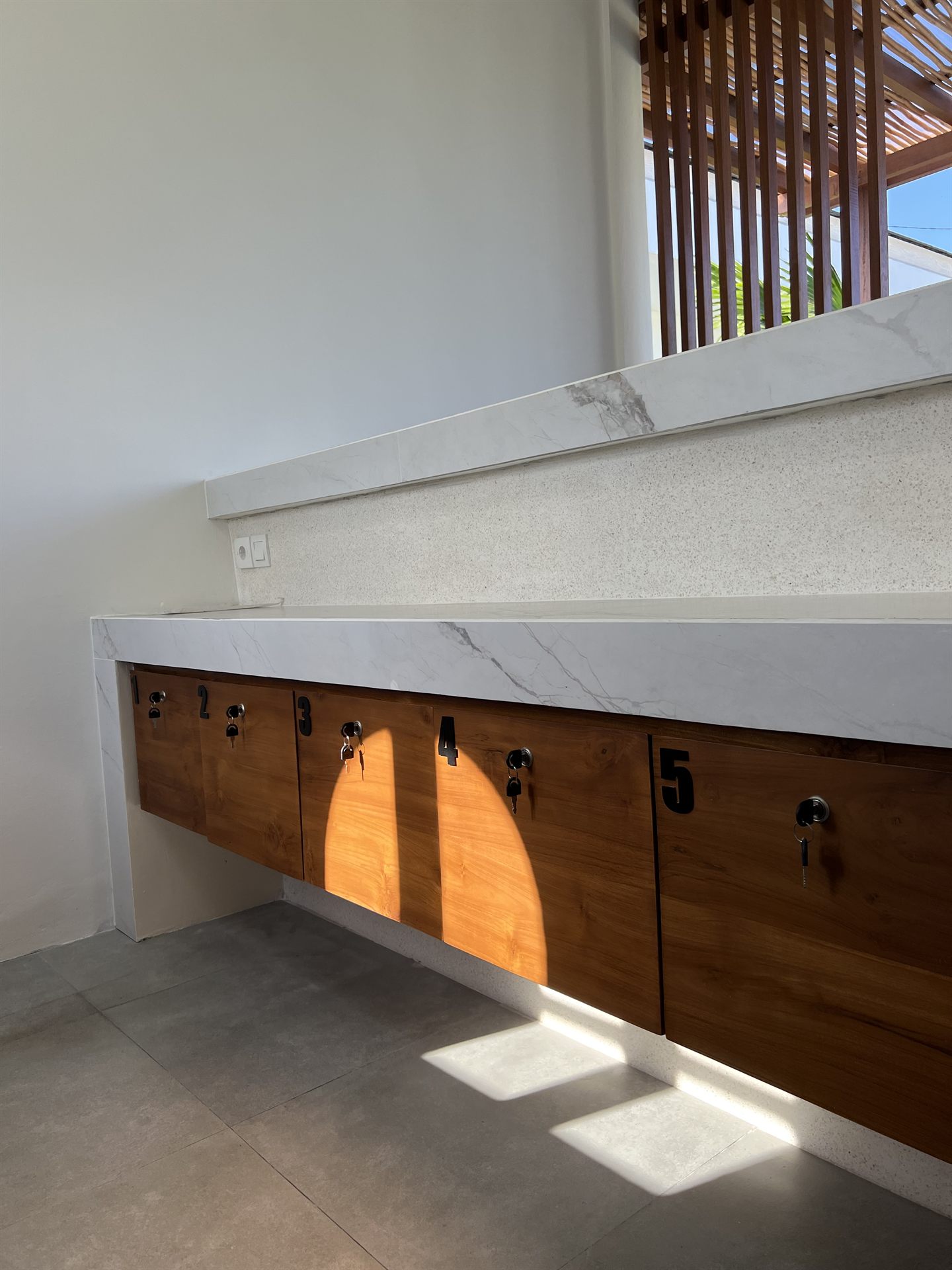 Sunlit marble counter with five numbered, lockable teak drawers, one per room